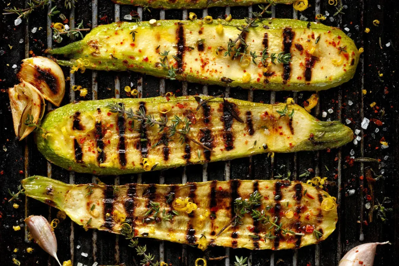 Perfekt gegrillte Zucchini-Scheiben mit Kräutern, Chili und Knoblauch auf dem Rost. Ein Genuss für jeden Grillmeister.