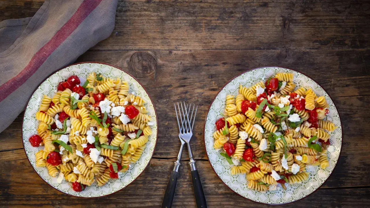 Zwei Teller mit leckeren schnellen Salaten ohne Mayo: Fusilli mit Kirschtomaten, Feta und Basilikum auf rustikalem Holztisch.