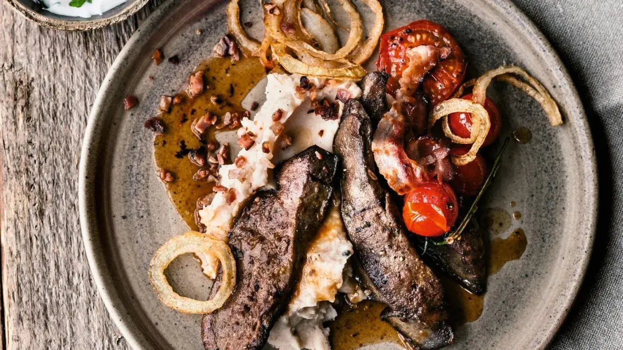 Herzhaftes leber braten mit Kartoffelpüree, Speck, Kirschtomaten und Röstzwiebeln auf einem rustikalen Teller.