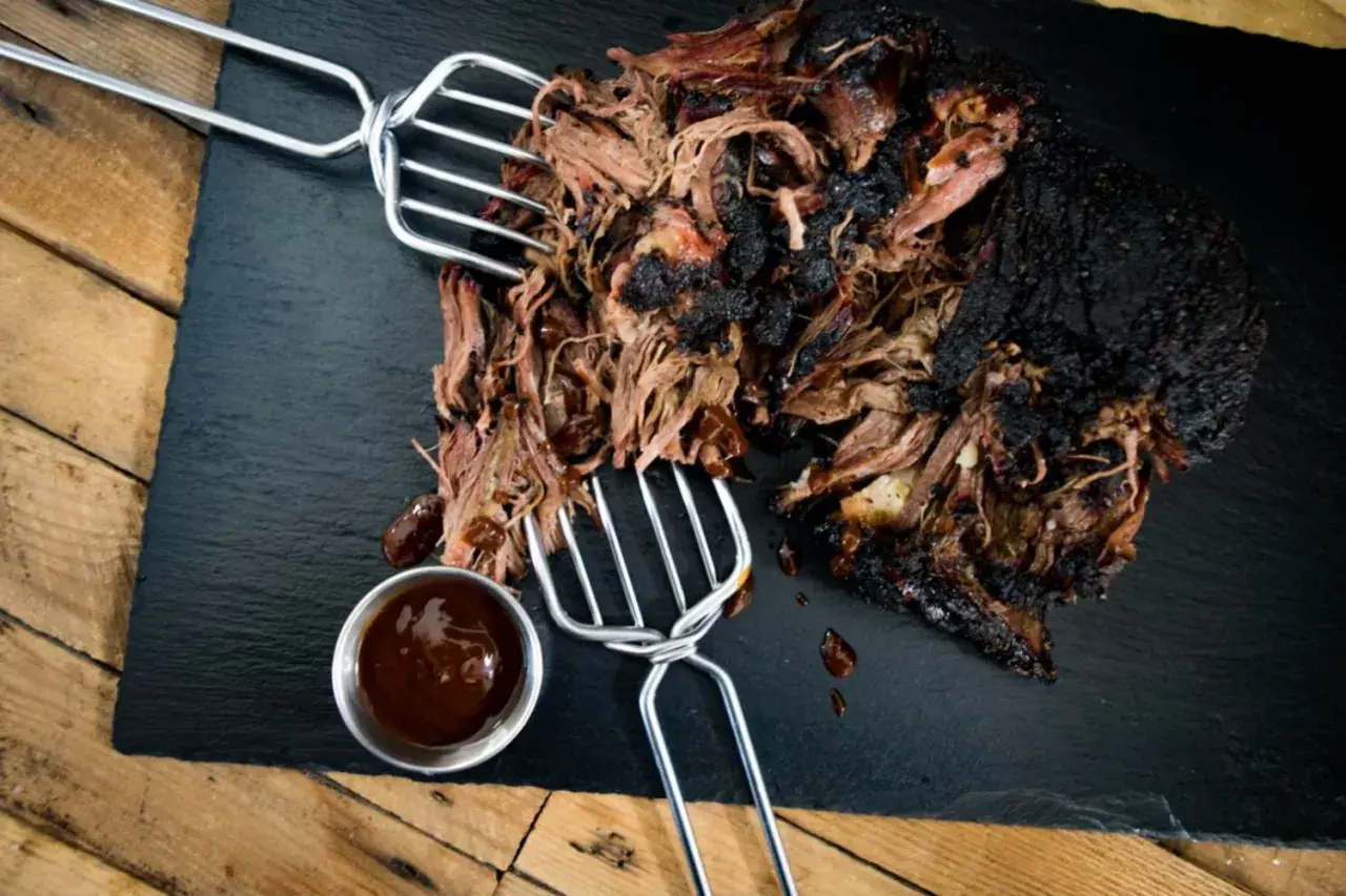 Zartes pulled beef mit dunkler Kruste, serviert mit BBQ-Sauce auf einem Schieferbrett.