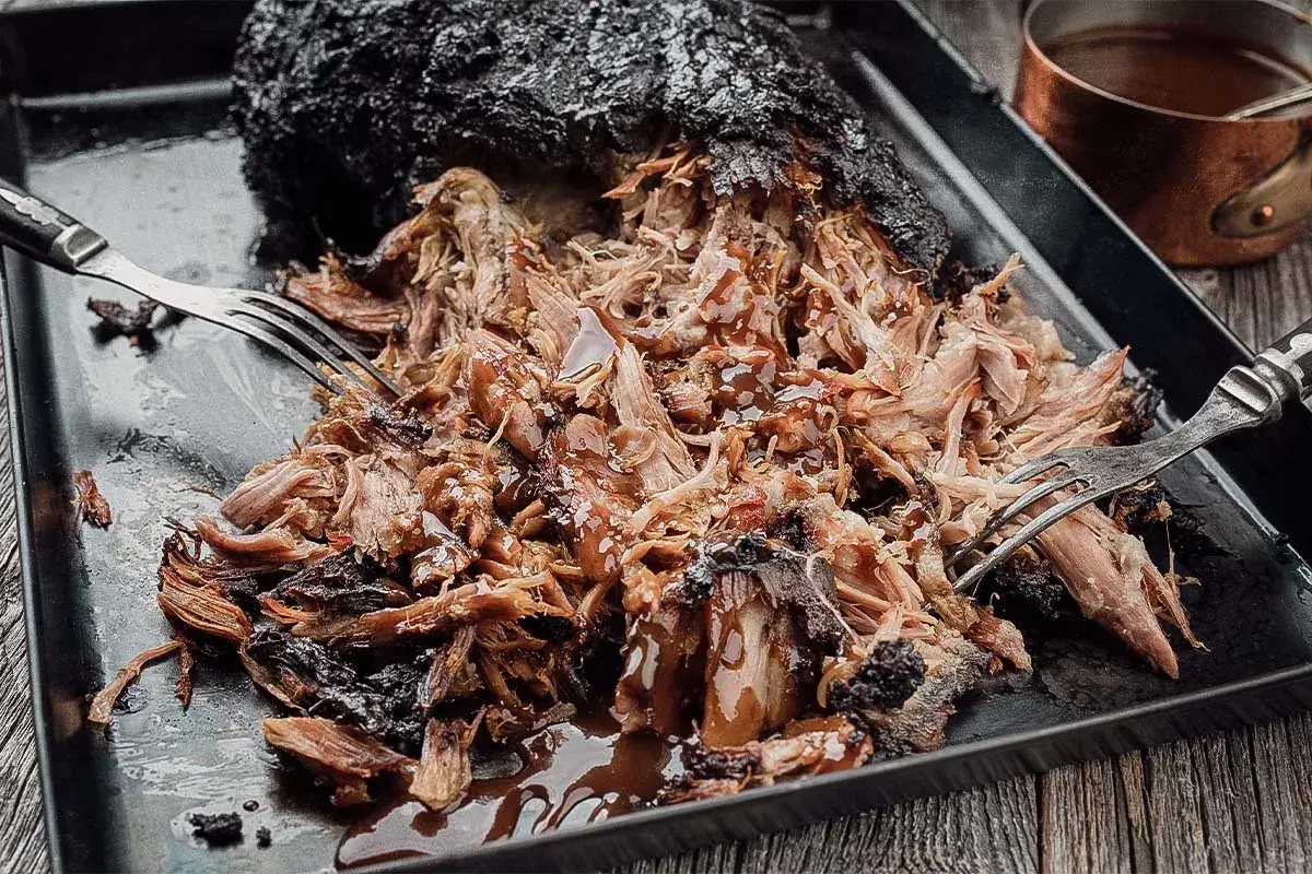 Saftiges Pulled Pork, frisch aus dem Smoker, mit einer dunklen Kruste und glänzender BBQ-Sauce. Zwei Gabeln zerreißen das Fleisch.