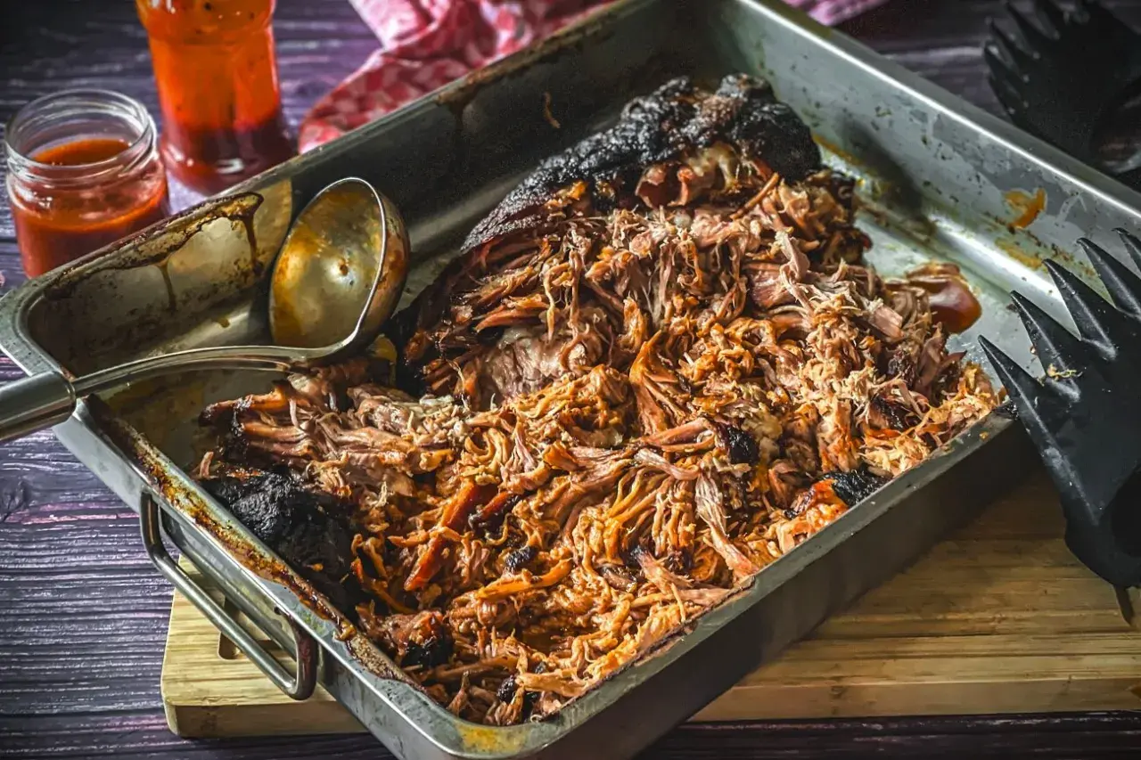 Saftiges pulled pork, frisch aus dem Gasgrill, in einer Metallschale mit Sauce und Fleischgabel.