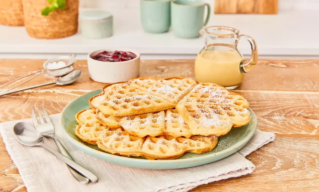 Leckere Waffeln ohne Ei, bestäubt mit Puderzucker, serviert mit Marmelade und Vanillesauce. Ein Genuss für jeden Tag!