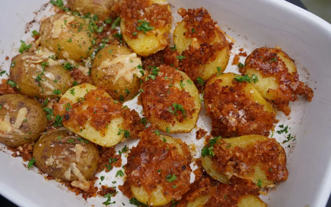 Knusprige parmesan kartoffeln mit Kräutern und grobem Salz bestreut, in einer weißen Auflaufform.