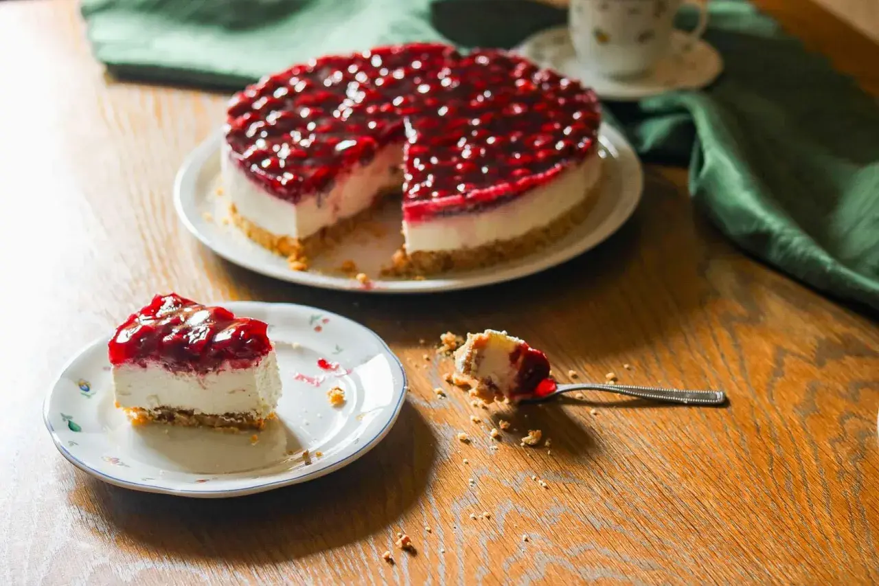 Ein köstlicher Kuchen ohne Backen mit Kirschtopping. Ein Stück auf einem Teller, ein Löffel mit einem Bissen daneben.