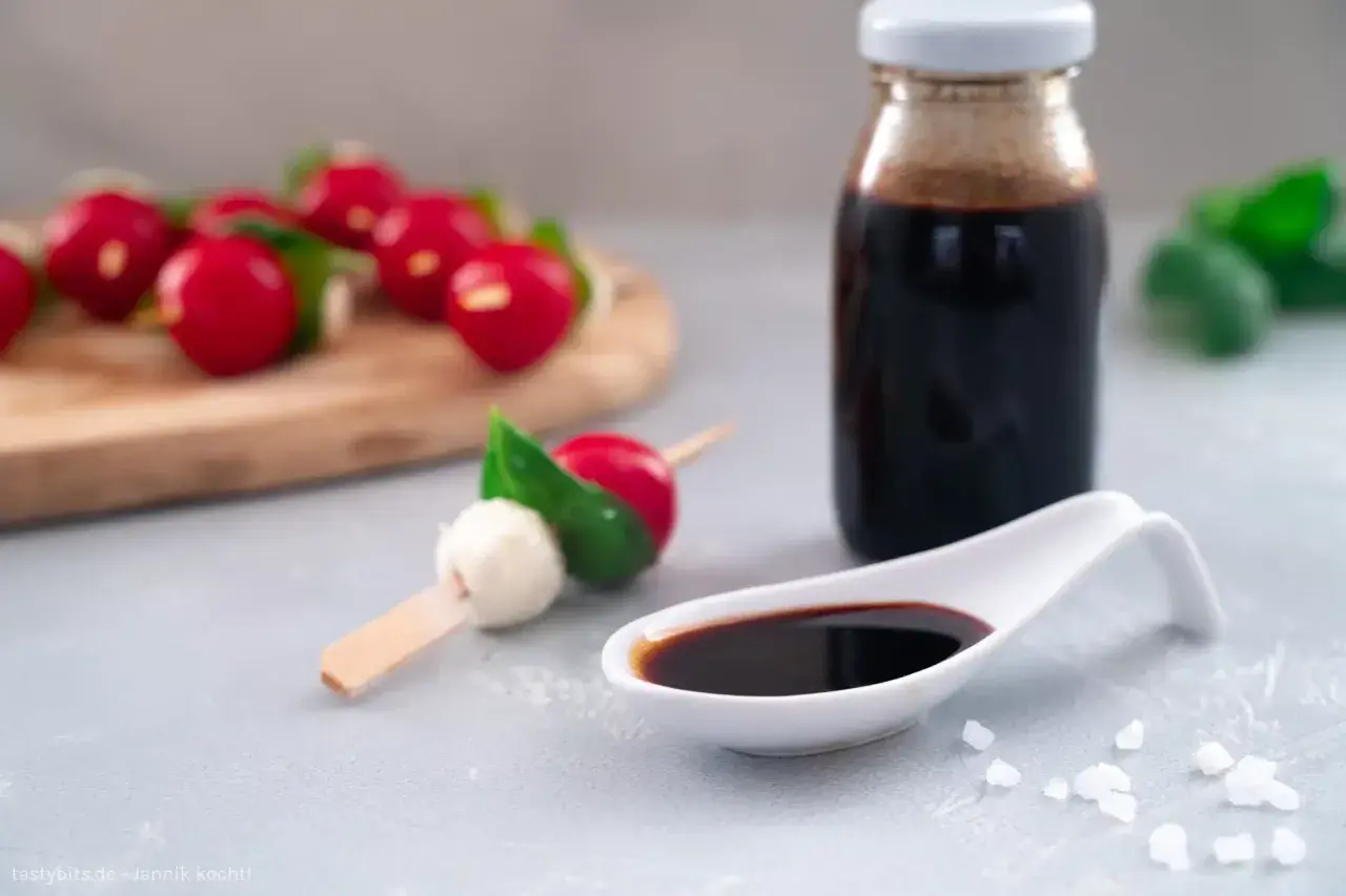 Ein Löffel mit dunkler balsamico creme, daneben eine Flasche und Radieschen-Mozzarella-Spieße.