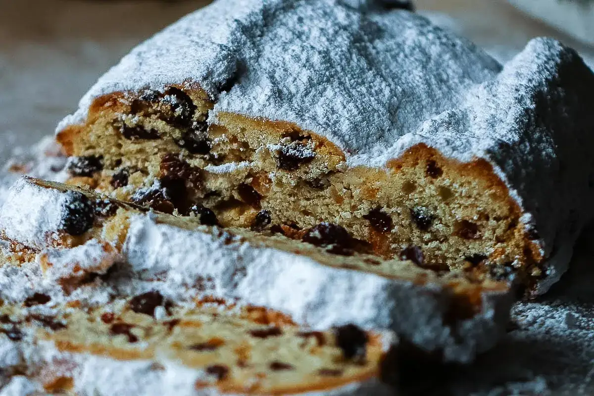 Ein saftiges Stollen-Rezept, das mit Puderzucker bestäubt ist. Rosinen und kandierte Früchte sind im Teig sichtbar.