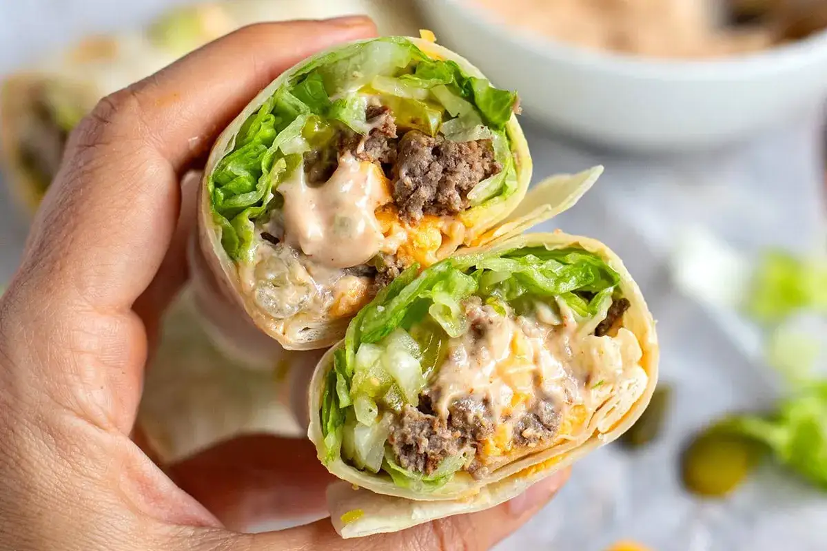 Eine Person h&auml;lt eine aufgeschnittene Big Mac Rolle mit Hackfleisch, Salat, K&auml;se und Sauce.