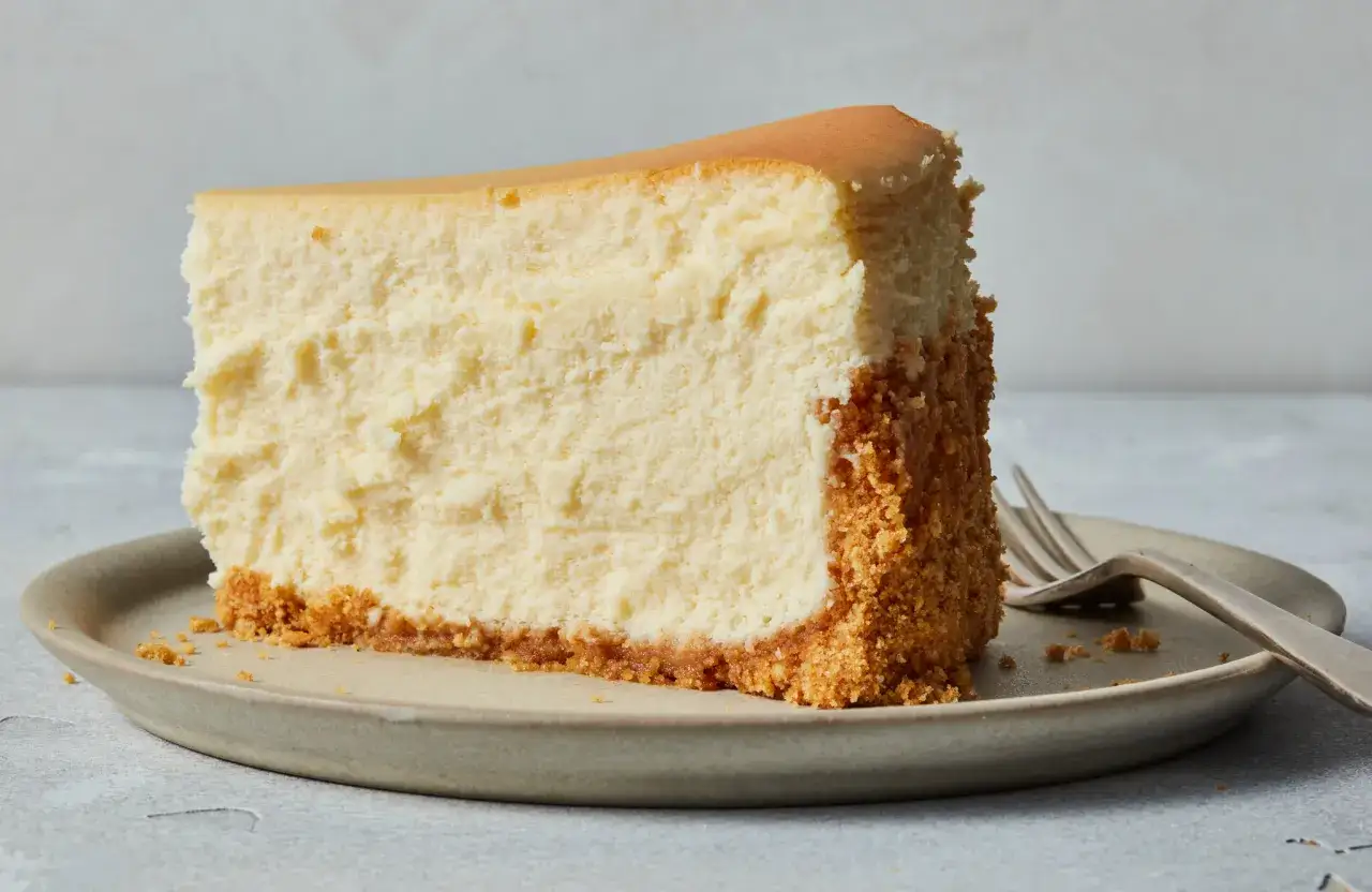 Ein cremiges Stück New York Cheesecake mit knusprigem Keksboden auf einem Teller, bereit zum Genießen.