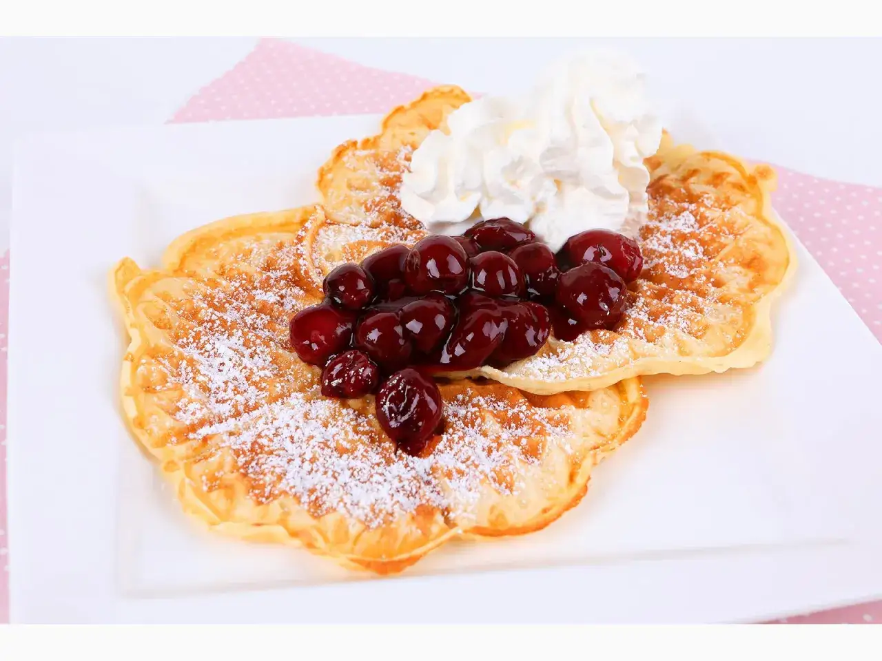 Zwei goldbraune Waffeln, best&auml;ubt mit Puderzucker, belegt mit Kirschen und Sahne. Ein perfektes Waffeln Rezept f&uuml;r den Genuss.