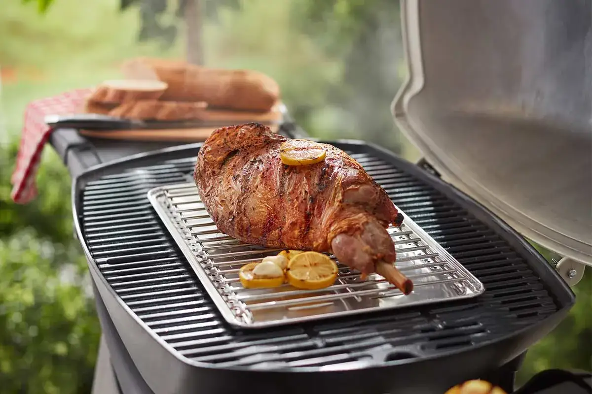 Ein saftiges Lammkeule wird auf einem Gasgrill zubereitet, mit Zitronenscheiben und Knoblauch garniert. Der Rauch steigt auf und verspricht ein k&ouml;stliches Gericht.