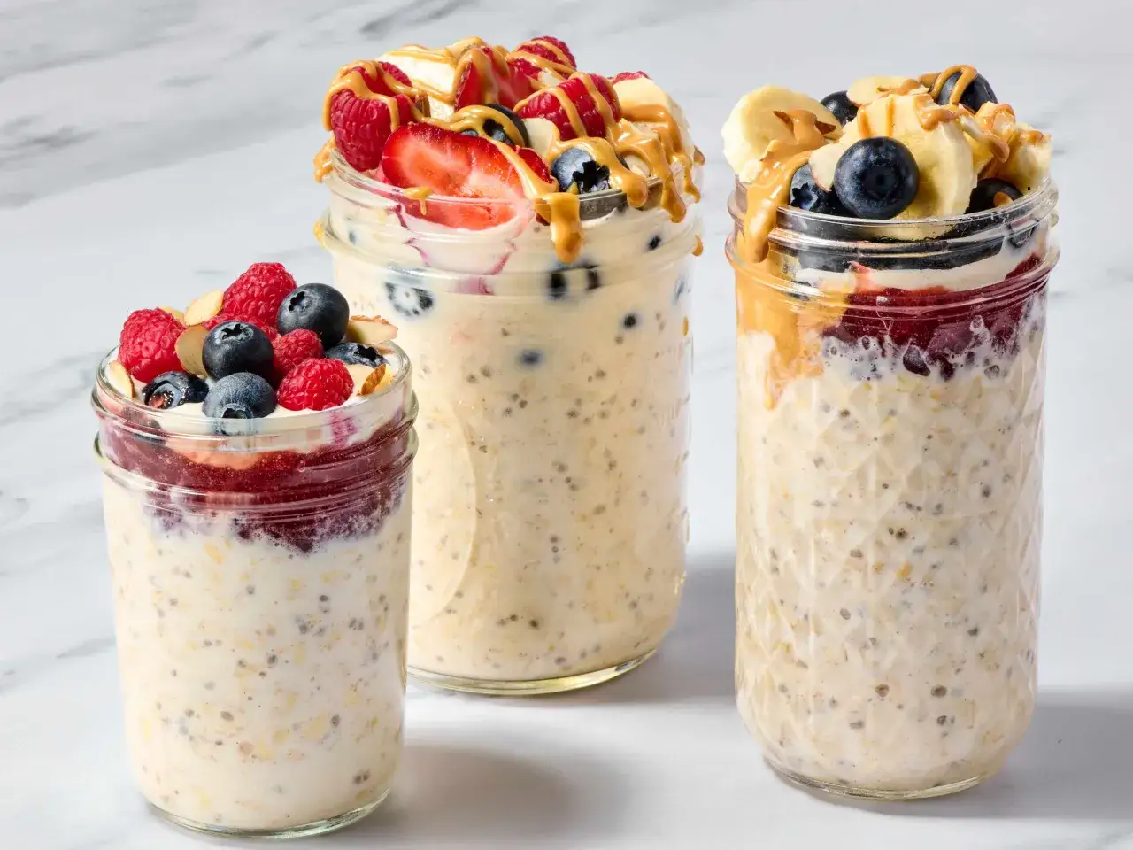 Drei Gläser mit Overnight Oats Grundrezept, garniert mit Beeren, Bananen und Erdnussbutter.