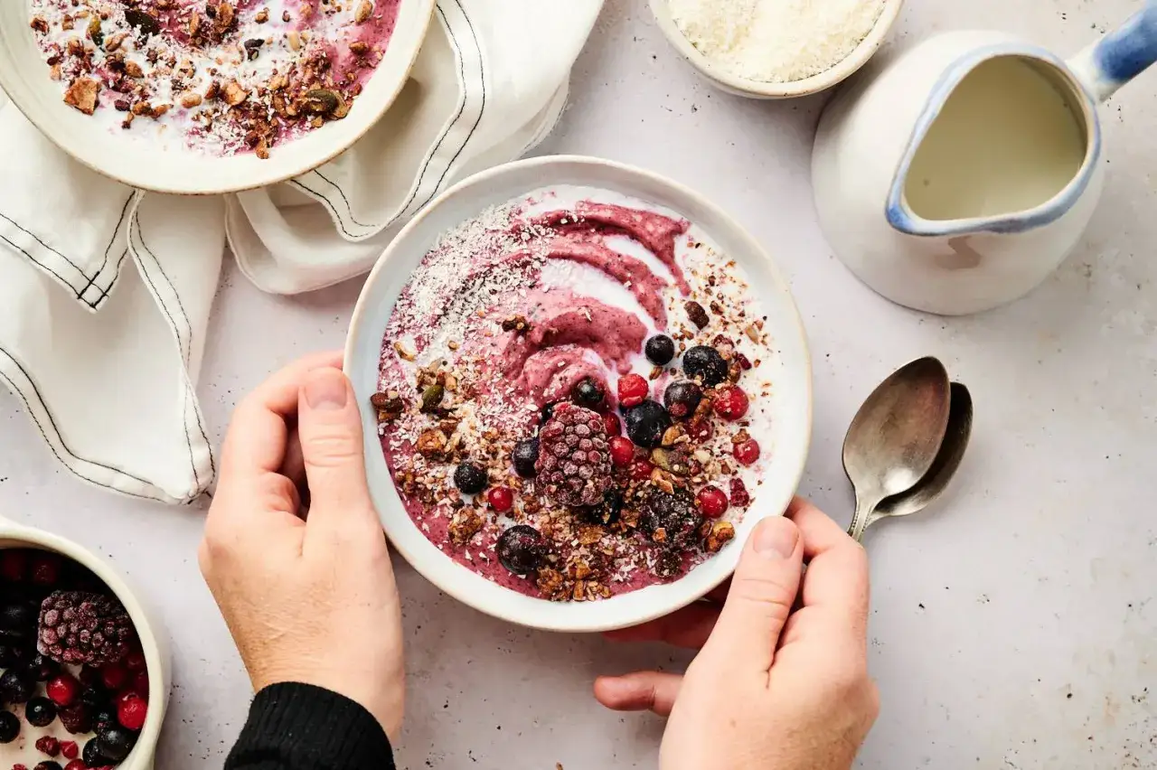 H&auml;nde halten eine Acai Bowl mit Beeren, Granola und Kokosraspeln. Ein einfaches Acai Bowl Rezept f&uuml;r einen gesunden Start.