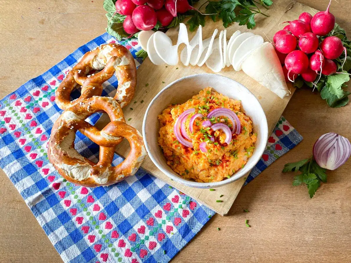 Leckeres Obazda Rezept mit Brezeln, Radieschen und Zwiebeln auf Holztisch.
