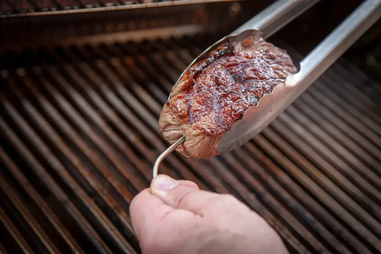 Ein saftiges Entrecôte wird mit einer Grillzange über einem heißen Rost gewendet. Perfekt für das Entrecôte grillen!