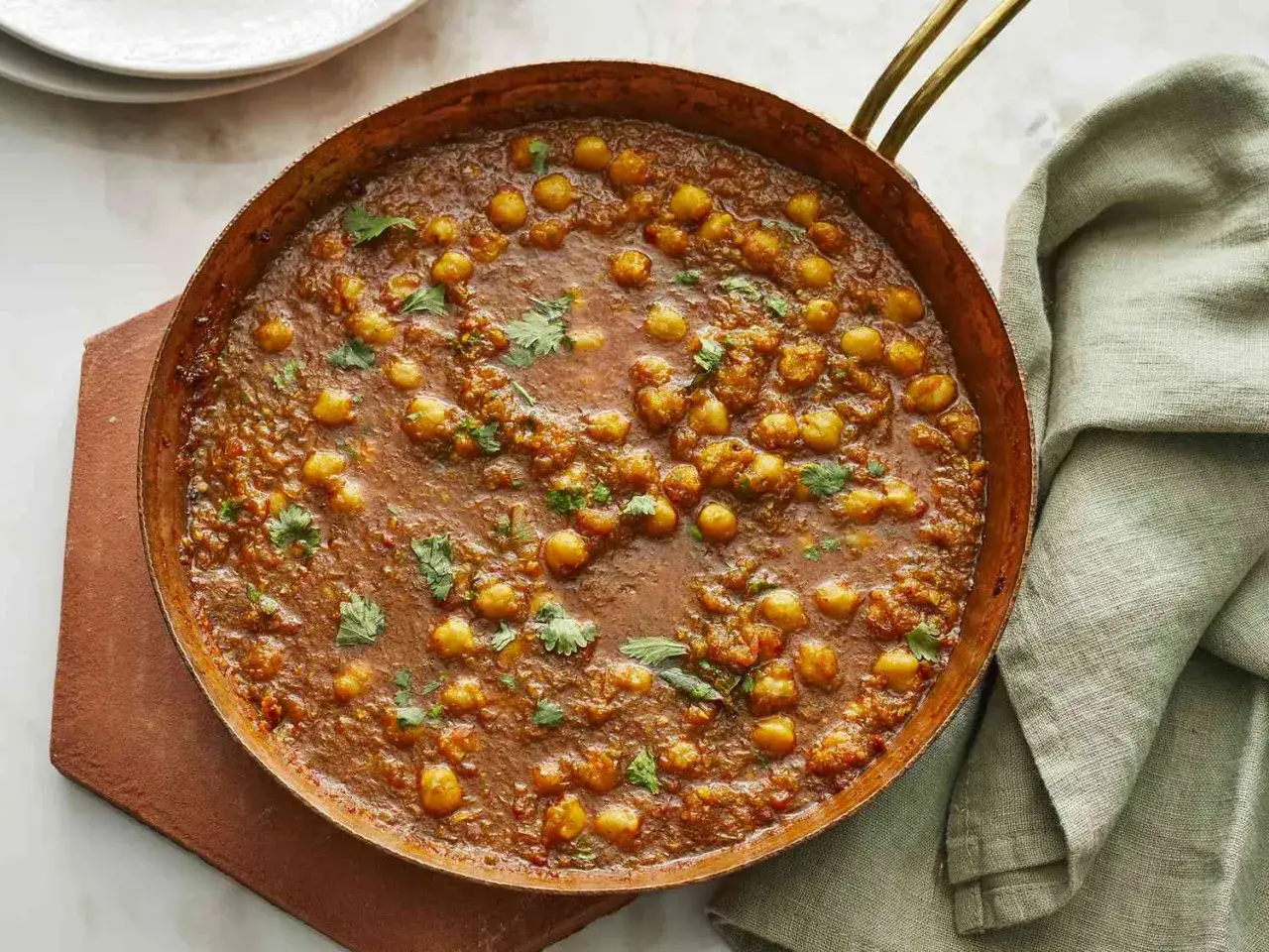 Ein k&ouml;stliches Chana Masala in einer Kupferpfanne, garniert mit frischem Koriander.