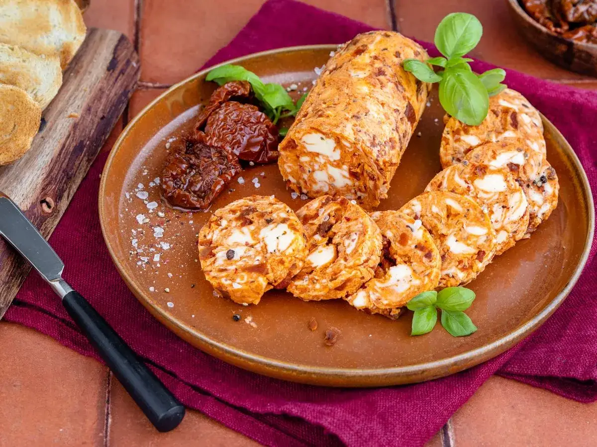 Tomatenbutter-Rezept: Ein Block und Scheiben von würziger Tomatenbutter mit getrockneten Tomaten und Basilikum auf einem Teller. Dazu geröstetes Brot.