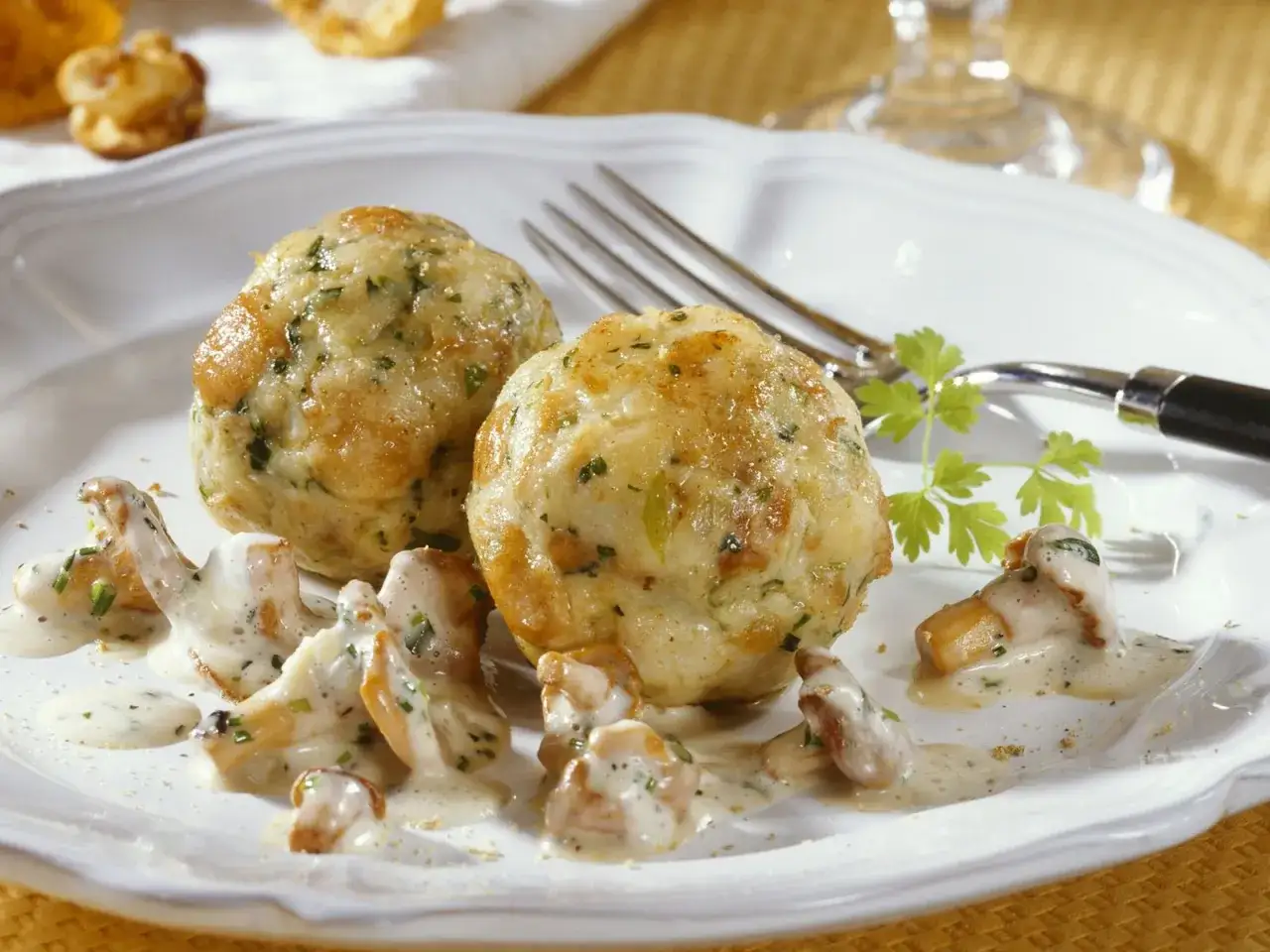 Zwei Klöße mit Pfifferling-Rahmsauce und frischer Petersilie auf einem weißen Teller.