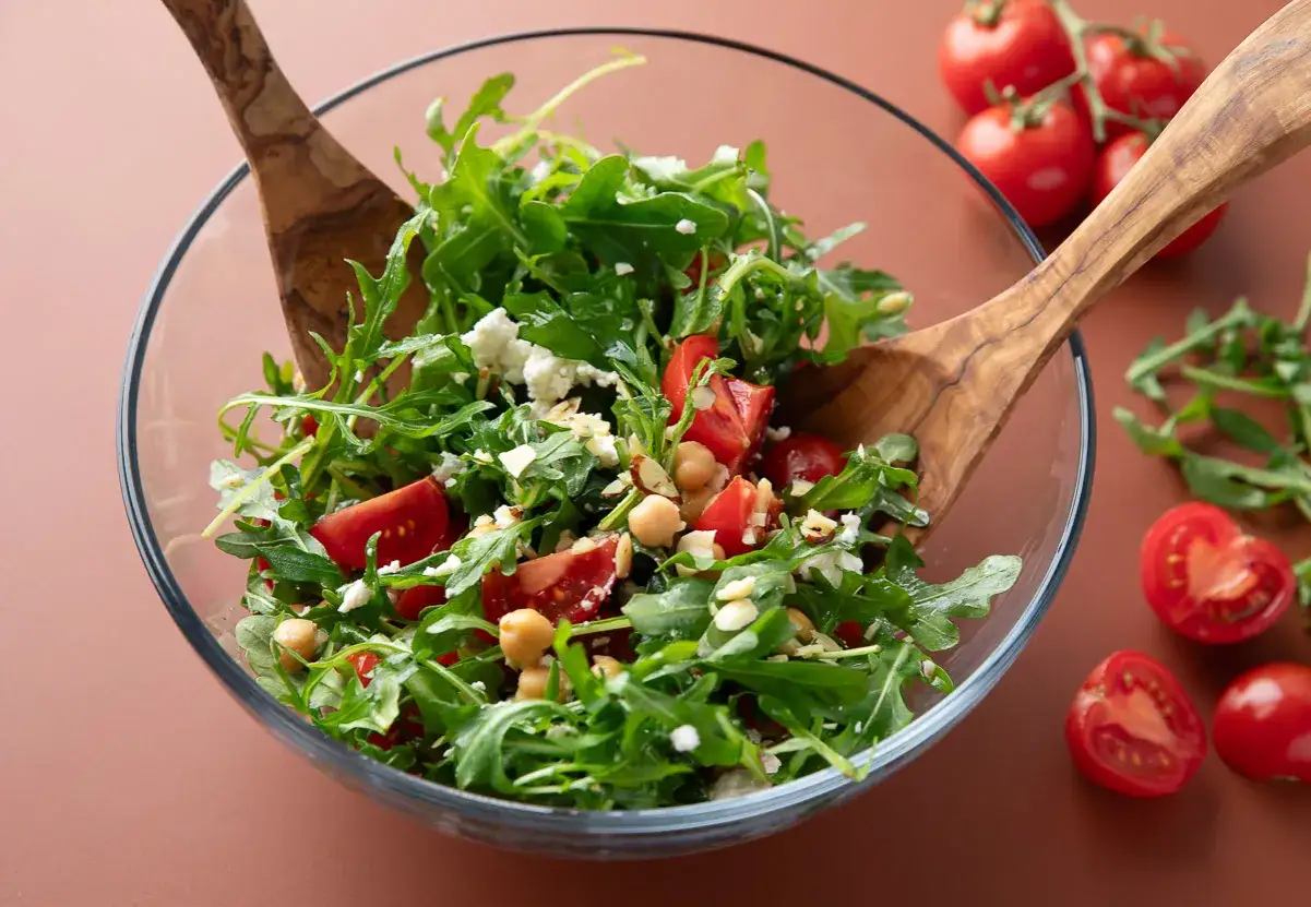 Frischer Rucola Salat mit Tomaten, Kichererbsen und Feta, gemischt mit Holzschaufeln.