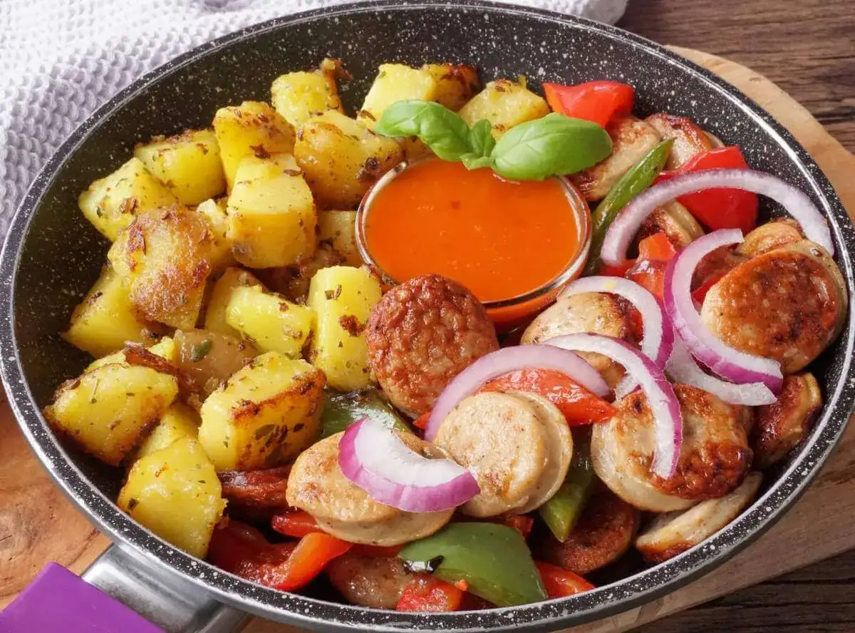 Bratwurst-Rezepte: Gebratene Kartoffeln, Wurstscheiben, Paprika und Zwiebeln in einer Pfanne mit Dip.