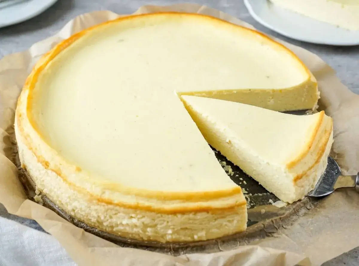 Ein cremiger Quarkkuchen ohne Boden, mit einem St&uuml;ck auf einem Tortenheber, bereit zum Servieren.