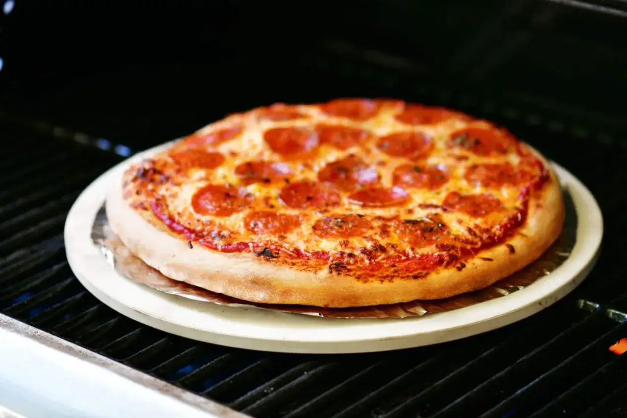 Eine k&ouml;stliche Pizza mit Pepperoni wird auf einem Pizzastein auf dem Gasgrill zubereitet. Der K&auml;se ist geschmolzen und die Kruste goldbraun.