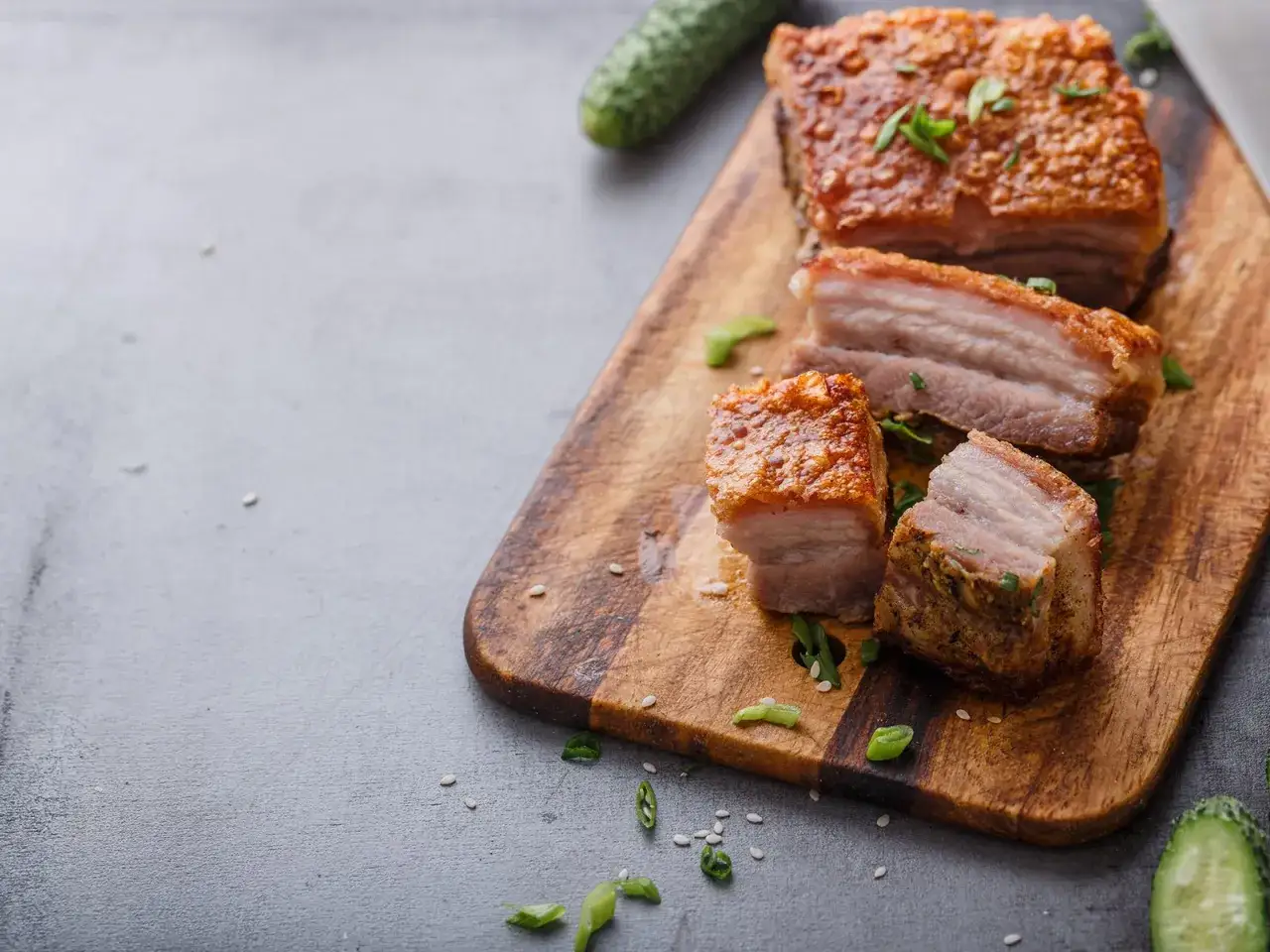 Knuspriger Schweinebauch, perfekt für Ihr nächstes schweinebauch rezept. Saftig und goldbraun auf einem Holzbrett, garniert mit Frühlingszwiebeln.