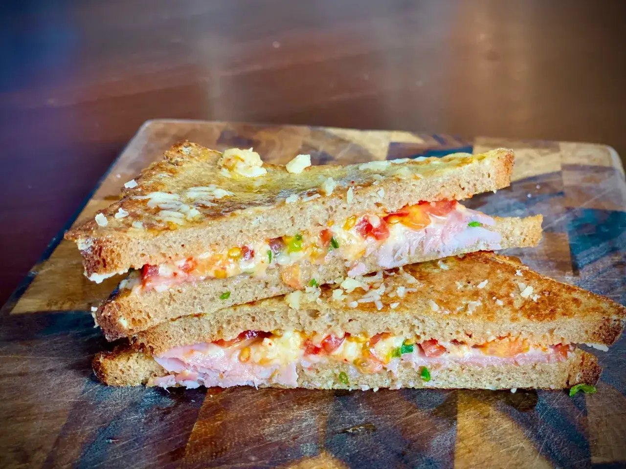 Zwei Dreiecke herzhaft belegtes French Toast mit K&auml;se, Schinken und Tomaten auf einem Holzbrett.