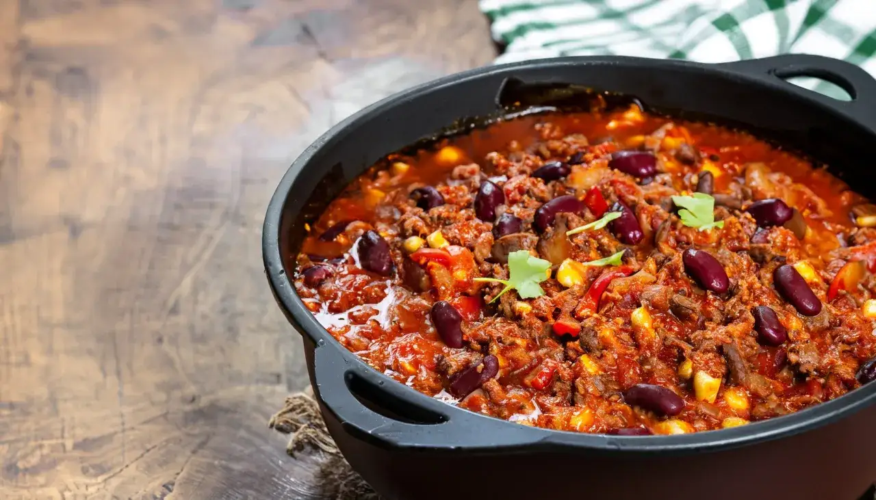 Herzhaftes Chili con Carne im Dutch Oven, mit Bohnen, Mais und Hackfleisch, bereit zum Servieren.