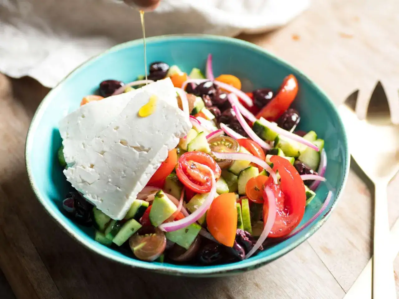 Frischer Tomatensalat mit Feta, Gurken, Oliven und roten Zwiebeln, betr&auml;ufelt mit Oliven&ouml;l.