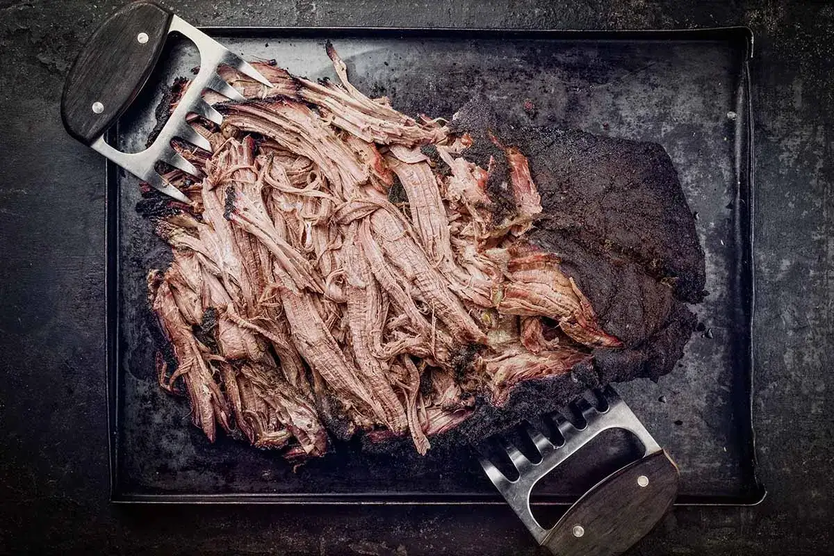 Zartes pulled beef, zerrupft mit Fleischkrallen, auf einem rustikalen Blech. Perfekt für BBQ-Liebhaber.
