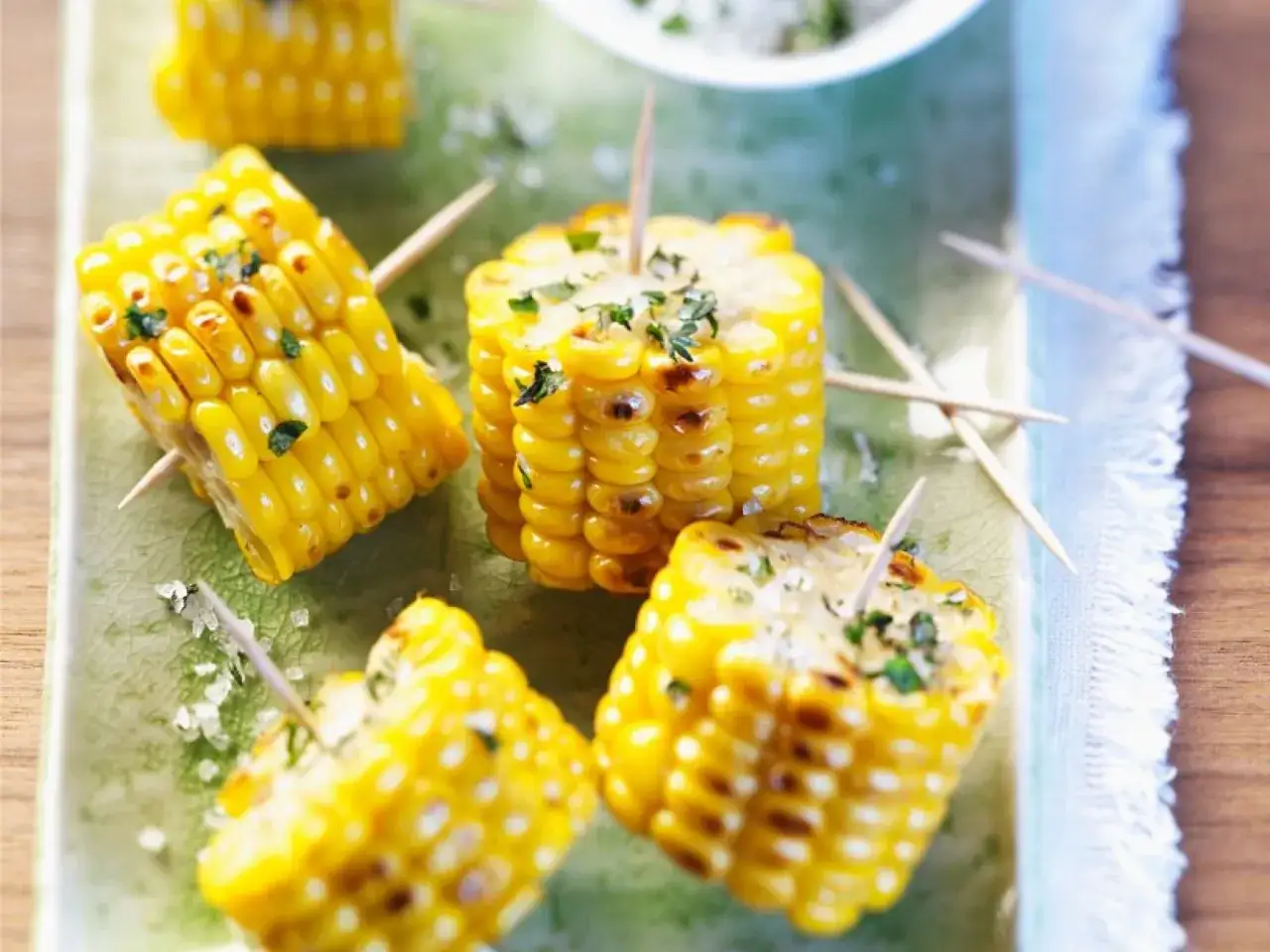 Kleine Stücke Maiskolben, gegrillt und mit Kräutern bestreut, auf einem grünen Teller. Perfekt zum maiskolben grillen!