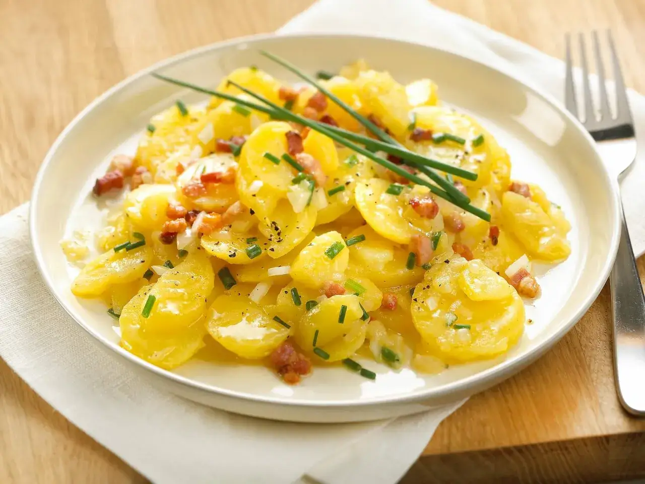 Ein Teller mit leckerem Kartoffelsalat mit Speck, garniert mit Schnittlauch und Zwiebeln.