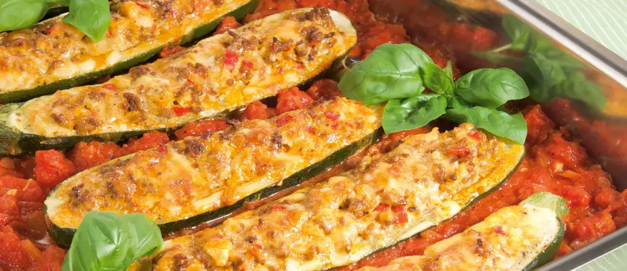 Gef&uuml;llte Zucchini mit Hackfleisch und K&auml;se &uuml;berbacken, serviert in einer Tomatensauce mit frischem Basilikum.