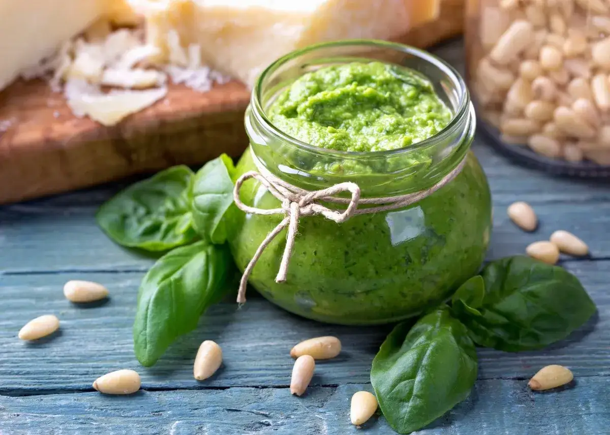 Frisches Pesto-Rezept im Glas, umgeben von Basilikum, Pinienkernen und Parmesan. Perfekt f&uuml;r Pasta!