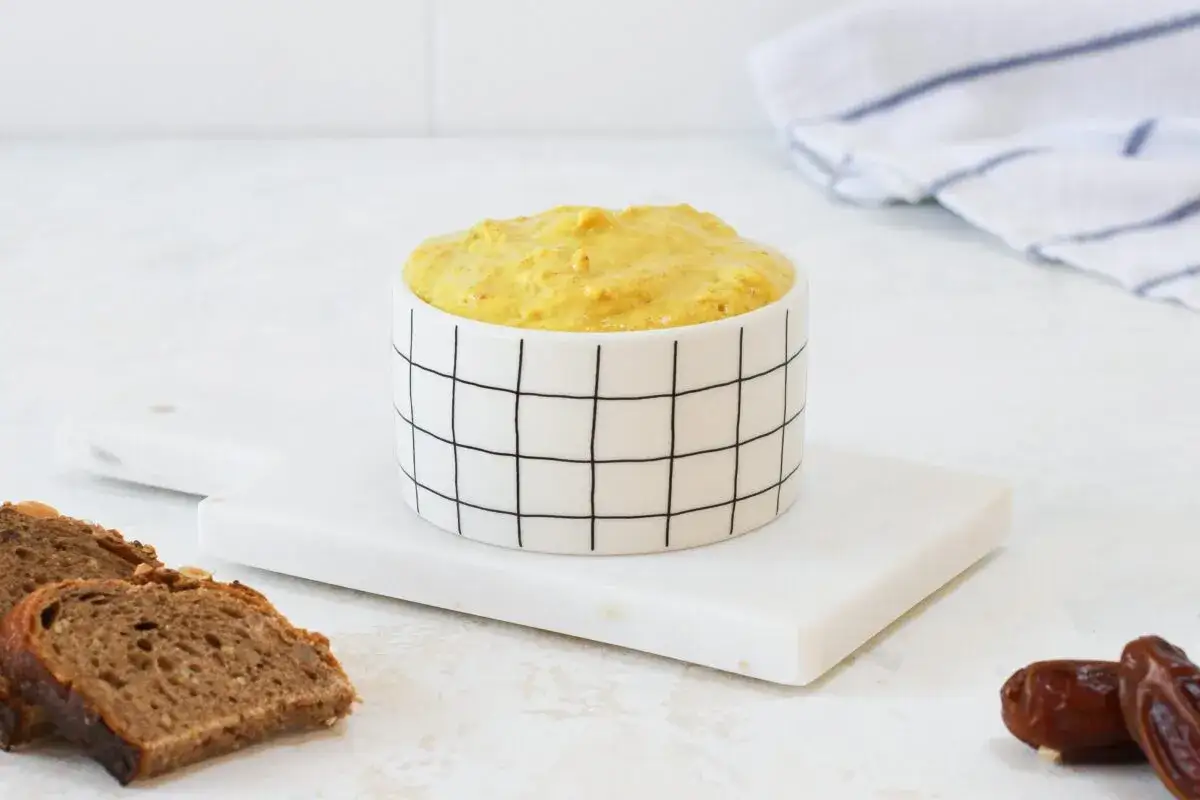 Ein cremiger curry dattel dip in einer modernen Schale, daneben Brot und Datteln.