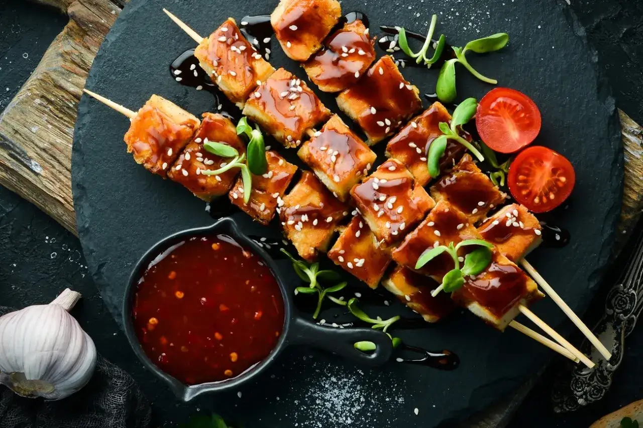 H&auml;hnchenspie&szlig;e mit gl&auml;nzender Teriyaki-Sauce, bestreut mit Sesam. Dazu eine Schale Sauce, Kirschtomaten und Knoblauch &ndash; ein tolles teriyaki sauce rezept.