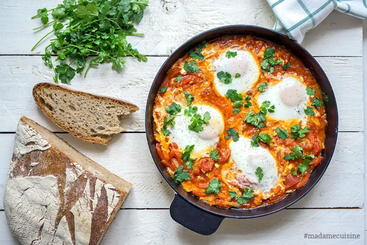 Herzhaftes Shakshuka-Rezept in einer Pfanne mit pochierten Eiern in Tomatenso&szlig;e, garniert mit Koriander. Dazu gibt es frisches Brot.