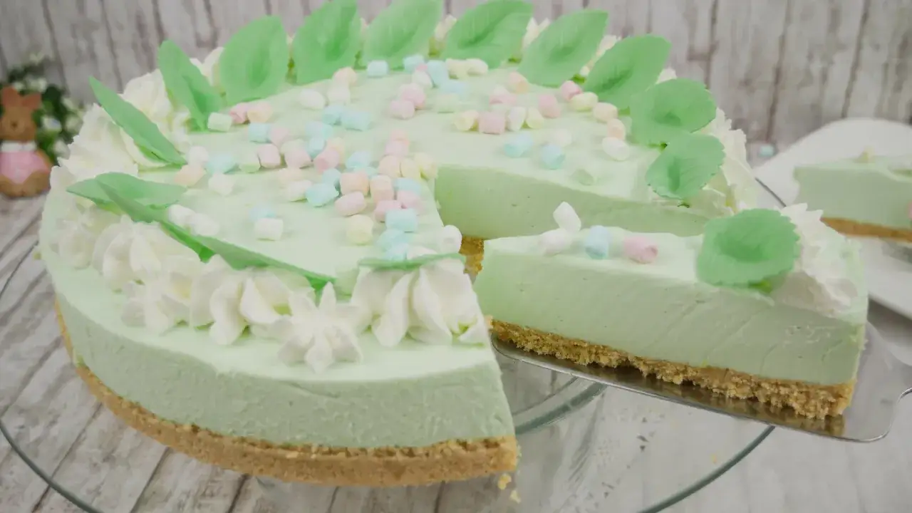 Eine helle, cremige Philadelphia Torte Waldmeister, dekoriert mit Marshmallows und grünen Blättern.