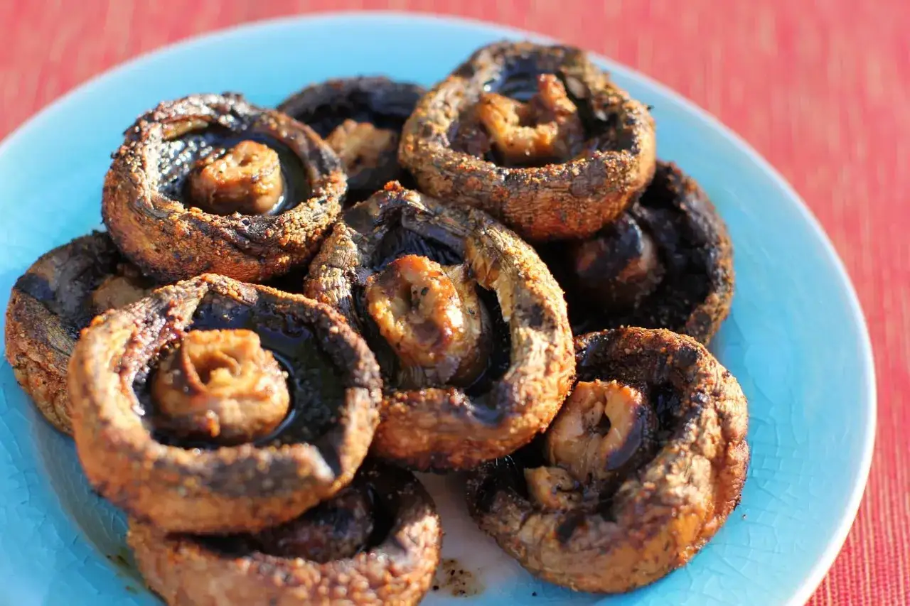Gegrillte Champignons, gef&uuml;llt und saftig, liegen auf einem blauen Teller. Ein k&ouml;stlicher Genuss f&uuml;r jeden Grillabend.