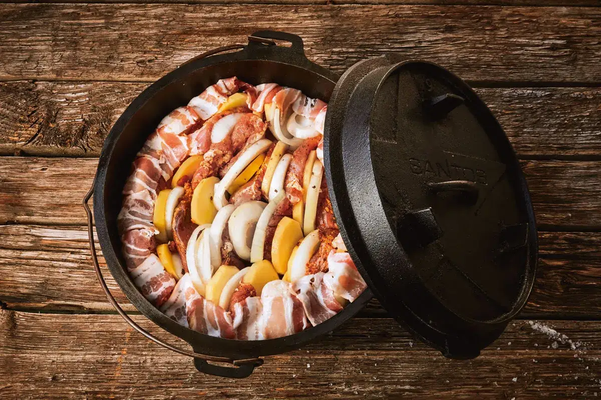 Schichtfleisch im Dutch Oven: Fleisch, Kartoffeln und Zwiebeln werden liebevoll geschichtet, bereit für ein deftiges Outdoor-Erlebnis.