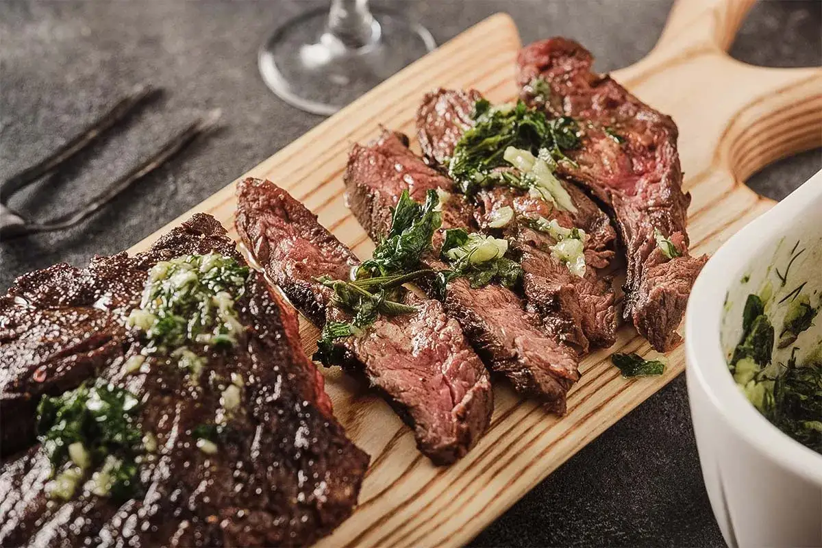 Saftiges, in Scheiben geschnittenes Flank Steak Deutsch, &uuml;bergossen mit Kr&auml;utersauce, auf einem Holzbrett serviert.