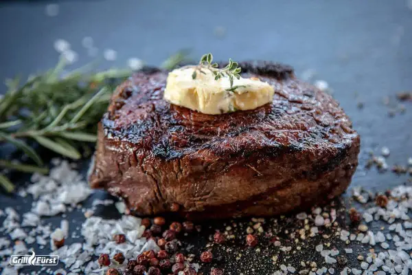 Perfekt gegrilltes Entrecôte mit Kräuterbutter, umgeben von grobem Salz und Pfefferkörnern. Ein Fest für Fleischliebhaber!