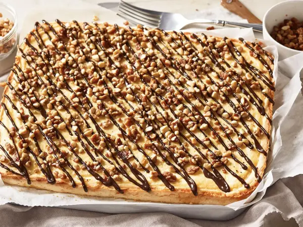 Ein rechteckiger "Friss dich dumm Kuchen" mit cremiger Füllung, garniert mit Nüssen und Schokoladensauce.
