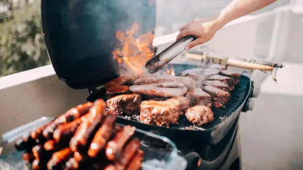 Fleisch und Würstchen brutzeln auf einem Grill auf dem Balkon. Die Frage, ob man auf dem Balkon grillen darf, wird hier mit Genuss beantwortet.